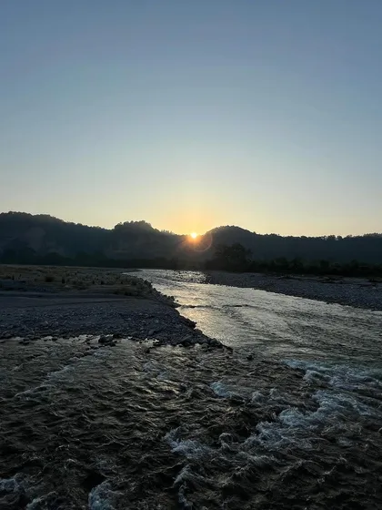 A tranquil sunrise over the river, with the sun just peeking over the hills. The cool, early morning light gives the scene a peaceful and quiet feeling.