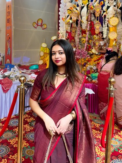 A close-up portrait against the backdrop of the Durga idol. The saree's color and texture stand out beautifully in the festive lighting.