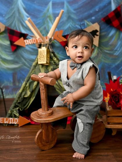 Ready for an adventure in the wild. This little explorer is all set for his camping-themed sitter session, featuring a forest backdrop and a cute wooden tricycle.