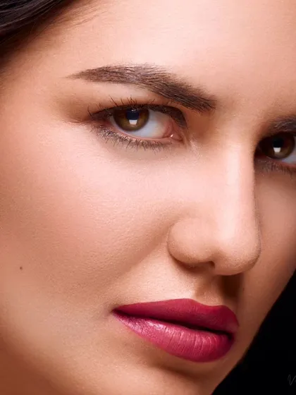 A powerful close-up beauty portrait. The model's direct gaze and the precise lighting create a striking image that emphasizes the bold lip color and perfectly defined eyebrows.
