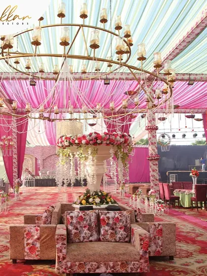 A multi-hued wedding tent with shades of pink and red. The space is filled with floral sofas and a grand central chandelier, creating a vibrant and luxurious environment.