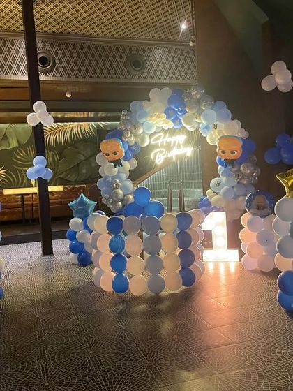 A "Boss Baby" themed decoration for a first birthday party. The setup includes balloon pillars, a cake table, and a large balloon arch.