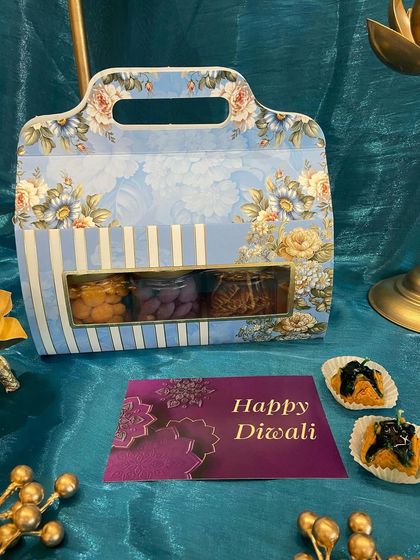 This floral-print carrier box with a window display offers a peek at the delicious treats inside. It's a charming and convenient way to gift assorted nuts and sweets for Diwali.