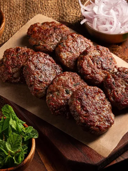 Perfectly seared Galouti kebabs arranged on parchment paper. The focus is on the texture and color of the meat, making it look juicy and delicious for a food delivery platform.