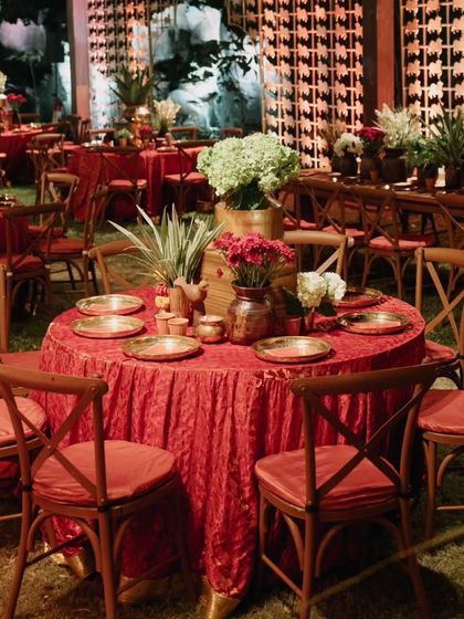 Round tables set with crushed red velvet tablecloths and simple floral centerpieces, offering a different seating arrangement within the same vibrant reception space.