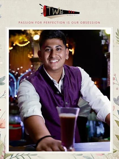 A smiling bartender with a dark, refreshing mocktail, ready to serve the next guest at the Mahalaxmi Lawns reception.