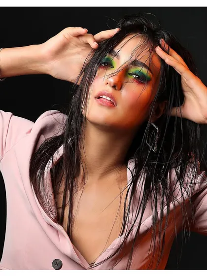 An experimental beauty portrait with a model in a pink blazer, featuring wet hair and vibrant, colorful eye makeup.
