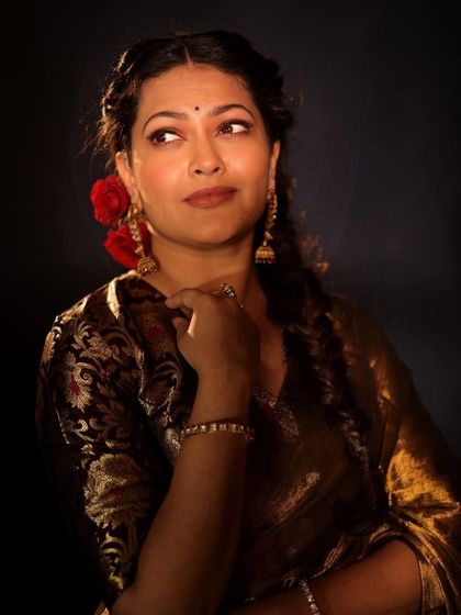 A classic retro portrait of Priyanka Barve, with braided hair, red flowers, and a beautiful brocade blouse.