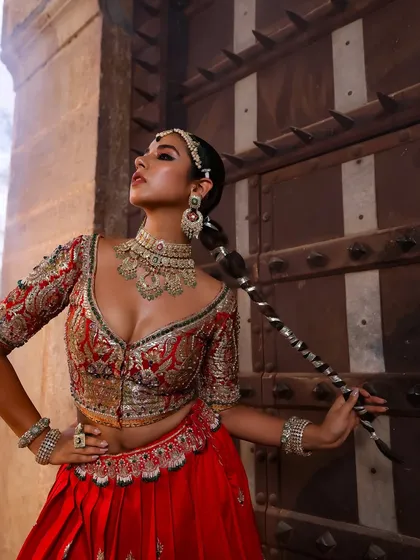 A powerful pose showing off the complete bridal look. The combination of the red lehenga, heavy jadau jewellery, and a dramatic braided hairstyle creates a look that is both traditional and fierce.