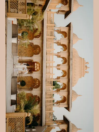 A wide shot capturing the majestic architecture of the palace. The couple stands together, a small but central part of a truly epic and royal scene.