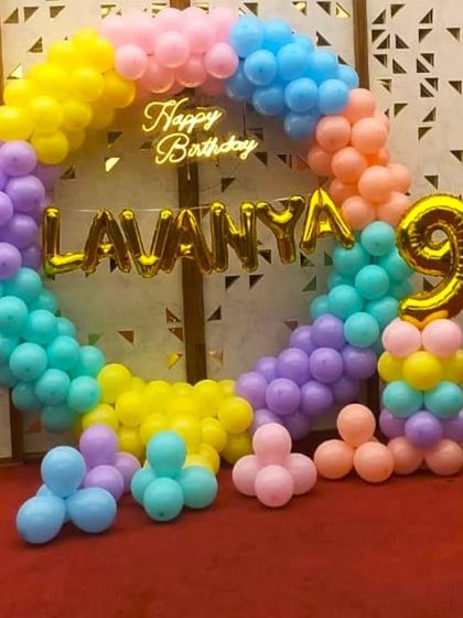 A colorful balloon ring for a 9th birthday celebration. The pastel rainbow balloons are accented with foil balloons for the name 'Lavanya' and the number '9', creating a personalized photo backdrop.