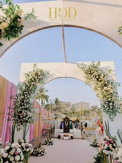 A beautiful entrance composed of white arches adorned with lush white and pastel flowers, creating a fresh, elegant, and inviting pathway.