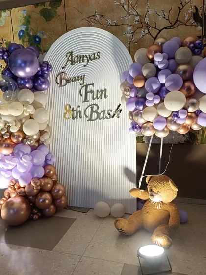 A "Beary Fun 8th Bash" for Aanya. This teddy bear theme uses a sophisticated color palette of lavender and rose gold balloons. A teddy bear holding a bunch of balloons adds a playful touch to the elegant setup.