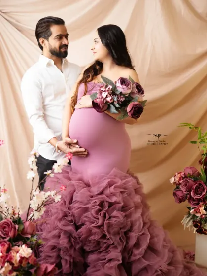 A beautiful maternity portrait featuring a mother-to-be in a ruffled mauve gown. The floral arrangements and soft lighting create a romantic and elegant setting.