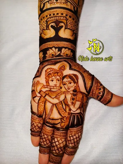 A beautiful portrait of Radha and Krishna, with Krishna playing the flute. This figurative work is a centerpiece on the palm, surrounded by swan and lotus motifs for a complete bridal look.