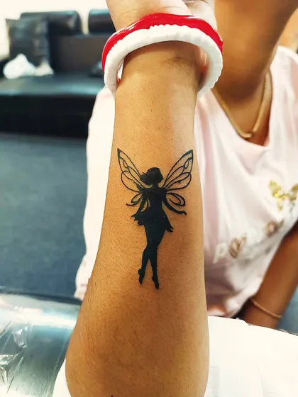 A solid black silhouette of a fairy on the forearm. This design combines minimalist principles with a touch of fantasy.