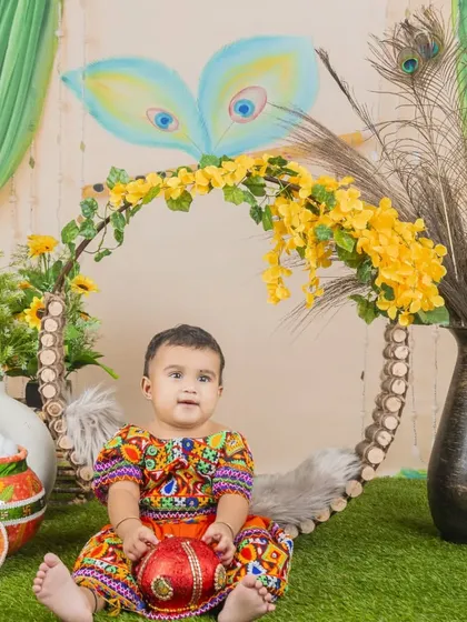 A creative Janmashtami setup with a baby girl dressed in a colorful outfit, sitting in a beautifully decorated swing.