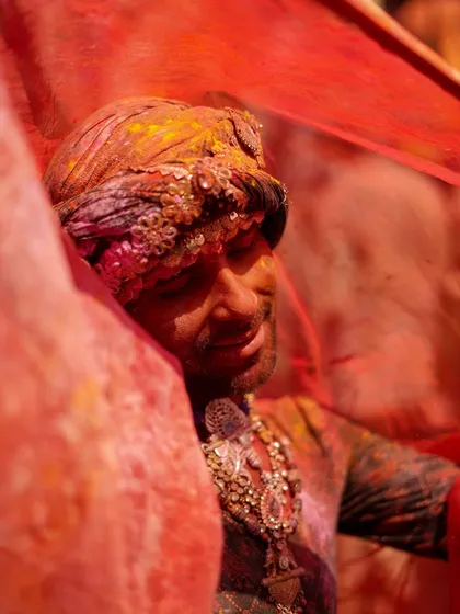 A man celebrating Lathmaar Holi, his face serene amidst a swirl of vibrant red fabric. This photo captures the personal, intimate moments of devotion found within the wild chaos of India's most colorful festival.