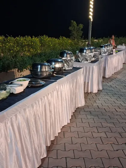 A long and clean buffet arrangement for an outdoor evening event. The tables are neatly skirted and all chafing dishes are arranged for easy access.