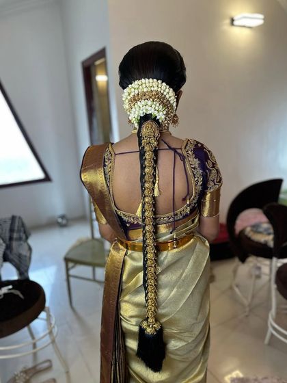 A full-length view of a bride in a golden silk saree. The traditional long braid with temple jewellery is the centerpiece of this classic muhurtham look.