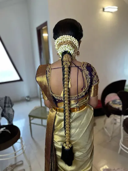 A full view of a bride ready for her ceremony. Her traditional braid is decorated with a full set of gold temple jewellery, perfectly complementing her gold and purple silk saree.
