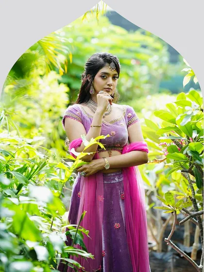 A full portrait of the lilac velvet lehenga set amidst lush greenery. The rich color and zardosi embroidery make it a standout choice for an evening event.