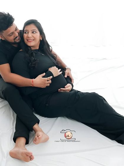A relaxed and intimate portrait of the couple lying on a white sheet in the studio. The partner embraces the mother-to-be from behind, creating a cozy and loving scene.