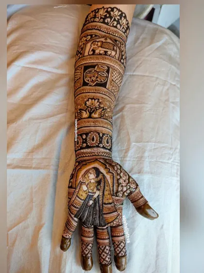 A beautiful bridal mehndi featuring a couple portrait. The design extends up the arm with classic motifs like elephants and lotus flowers, telling a story of love and tradition.