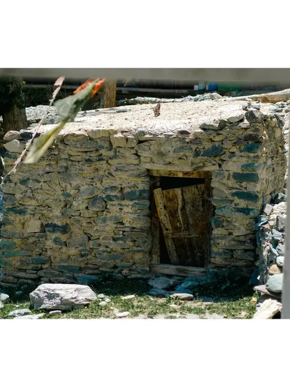 A weathered stone structure with a wooden door, framed through a window, offering a layered perspective of the village.
