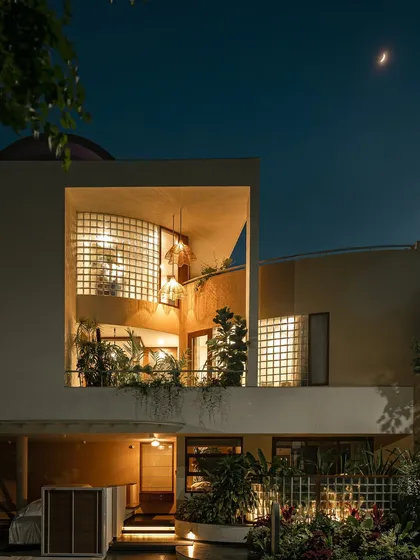 A wider perspective of the home at dusk. The illuminated balcony garden and lower-level planting work together to create a cohesive landscape design that envelops the entire structure.