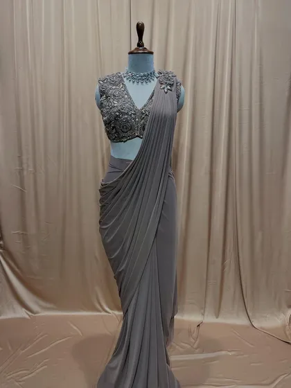 A classic drape saree in a subtle grey tone, paired with a sleeveless blouse fully embroidered with intricate floral patterns.