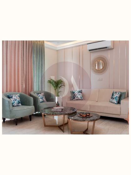 A full view of the living area featuring our bespoke furniture. The pastel green armchairs, beige sofa, and nested marble coffee tables were all selected and placed to create a harmonious and elegant setup.