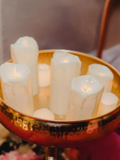 A close-up of a brass bowl filled with pillar candles. We use candlelight extensively in our decor to create a warm, romantic, and intimate atmosphere, especially for evening events.