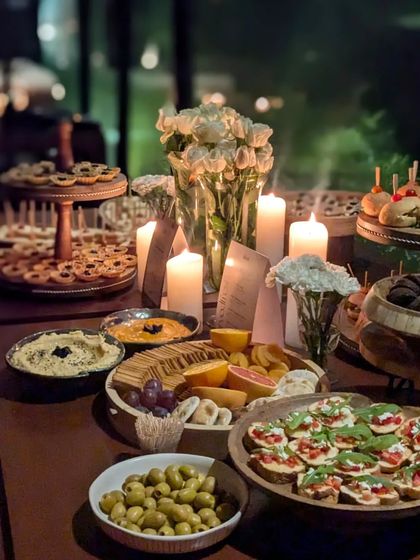 A candlelit evening spread. This grazing table creates a warm and inviting ambiance with an assortment of olives, bruschetta, cheese platters, and desserts, perfect for an intimate gathering.