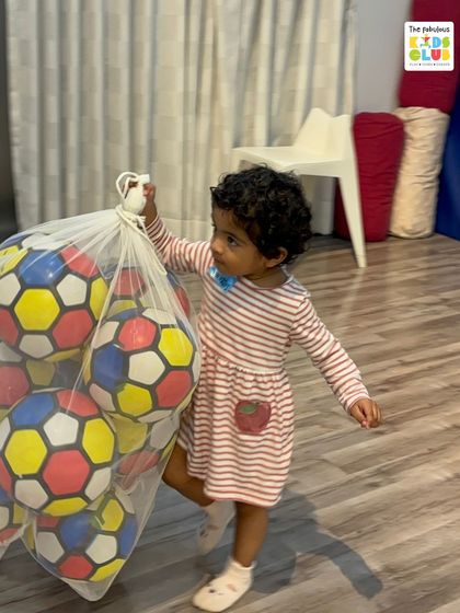 A toddler confidently carries a large bag of balls. This small act shows the independence and physical confidence that children develop through our activities.
