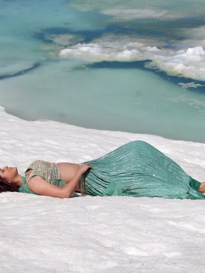 A wide shot showing the contrast of the green lehenga against the white snow and blue water.