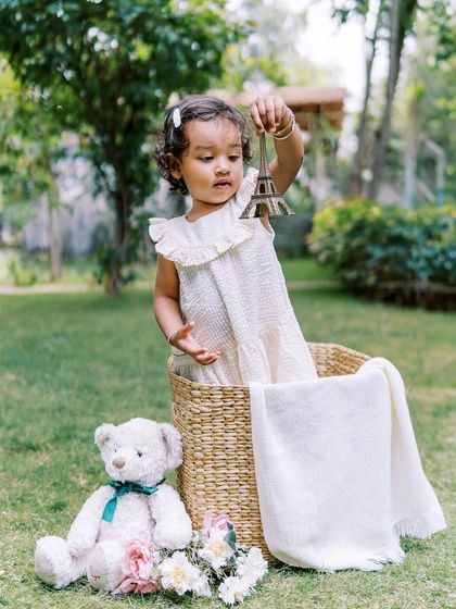 A little girl in a basket, holding a miniature Eiffel Tower. A whimsical and creative shot from a second birthday session.