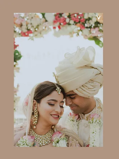 A close-up portrait filled with joy and tenderness. The bride's happy smile and the groom's loving gaze are perfectly framed under a floral arch.