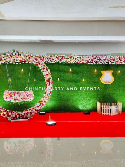 A beautiful naming ceremony stage with a floral swing against a faux grass wall. The circular floral frame creates a perfect photo opportunity.