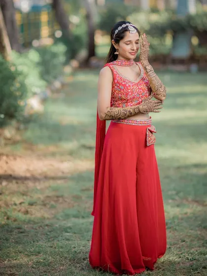 A full-length portrait of the bride during her Mehendi ceremony, dressed in a vibrant red outfit.