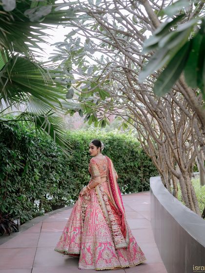 A graceful shot of the bride walking away, giving a glimpse of her complete bridal look from the back. The lush green pathway provides a perfect natural frame.