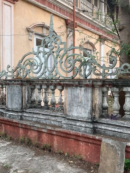 The weathered but ornate boundary wall of the palace, featuring intricate metalwork and stone pillars that hint at its former grandeur.