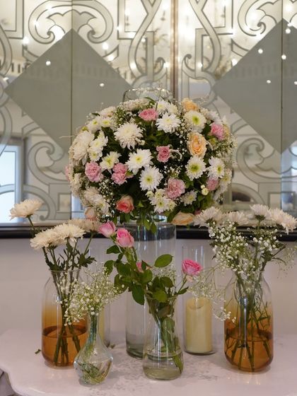 A simple yet beautiful centerpiece detail. A large bouquet of white and pink chrysanthemums and roses is surrounded by smaller glass vases, creating a delicate and fresh look for the tables.