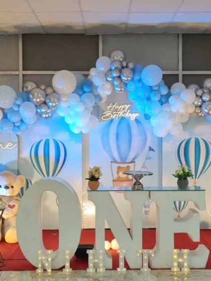 A wide shot of a hot air balloon first birthday party, showing the full scale of the decoration in a banquet hall.