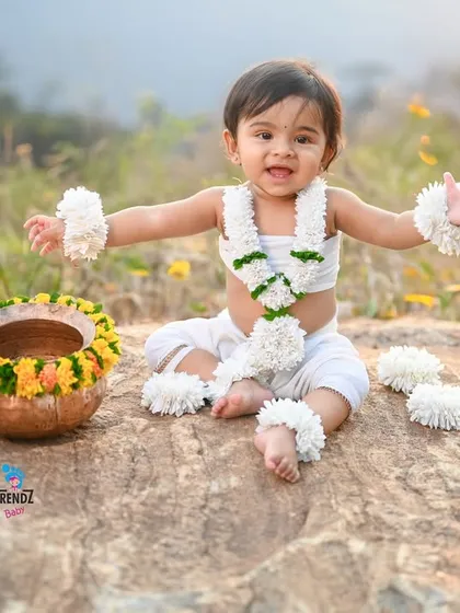 A full, edited shot from an outdoor session. The baby is dressed in a lovely floral outfit, sitting on a rock in a field of wildflowers.