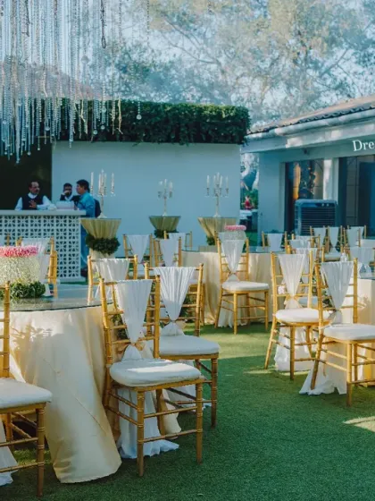 A wide view of the guest seating at an outdoor wedding. The gold chiavari chairs and cream-colored linens provide a classic and elegant look that complements the lush green lawn.