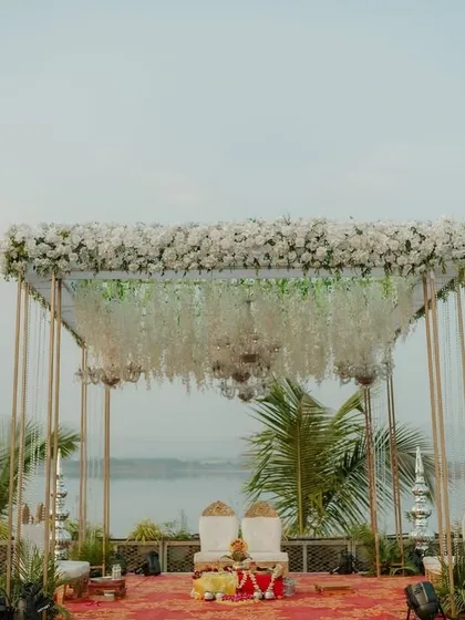 A minimalist mandap with a maximalist view. I designed this elegant structure with a canopy of white florals and hanging crystals to perfectly frame the serene lakeside backdrop, blending nature with sophisticated design.