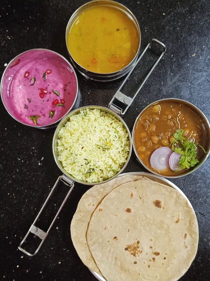 A top-down view of a packed tiffin, showing the different components like ghee rice, chole, dal, and beetroot raita, ready to be enjoyed with soft rotis.