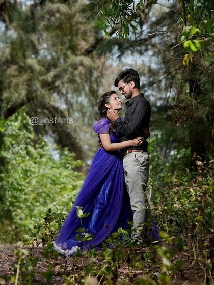 A romantic pre-wedding embrace in a lush, green forest. The deep blue color of the gown stands out beautifully against the natural backdrop.