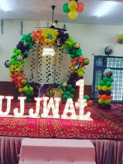 A jungle theme stage decoration for a first birthday party. I used marquee letters to spell out the name 'UJJWAL' and created a balloon arch with animal characters.